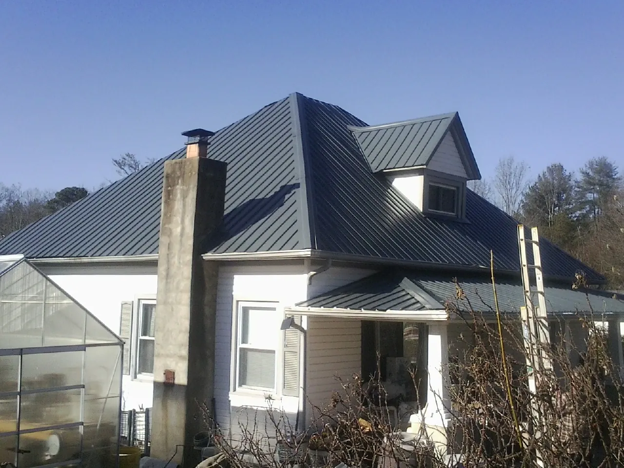 Dark blue standing seam metal roof on a white farmhouse with dormer — Slate & Tile Roof Repair by Roofing Brothers in Caledonia