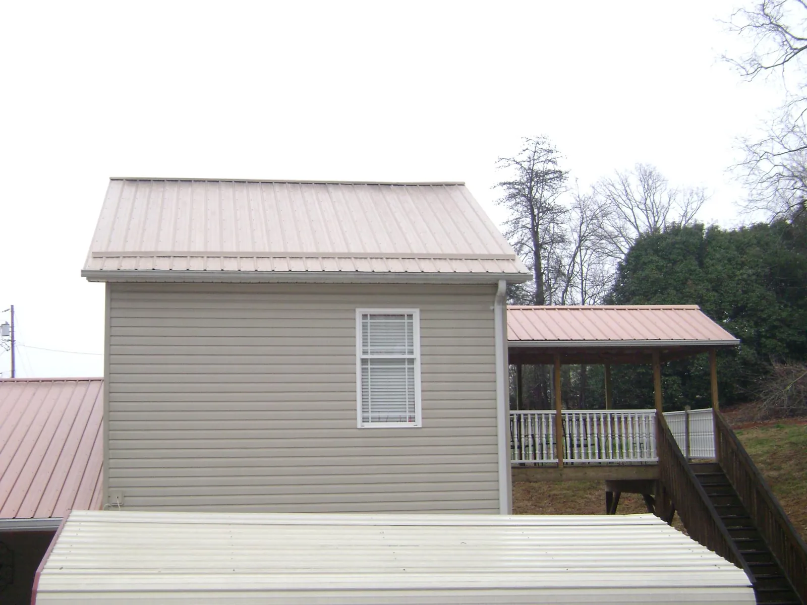 Tan metal roofs on a two story addition and attached porch, from a Roof Replacement job in Caledonia